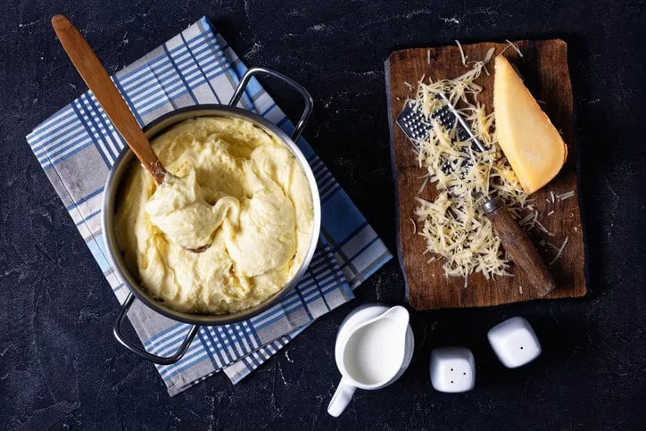 aligot, cheesy mashed potato dish in a metal pot with wooden spoon on a concrete kitchen table, with ingredients, french cuisine, horizontal view from above, flat lay