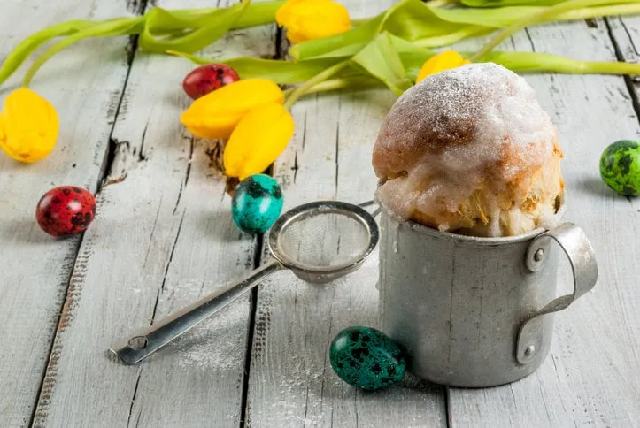 spring holiday easter  easter cake in a rustic metal mug, decorated with icing and powdered sugar, colored eggs and flowers tulips on the wooden table, copy space