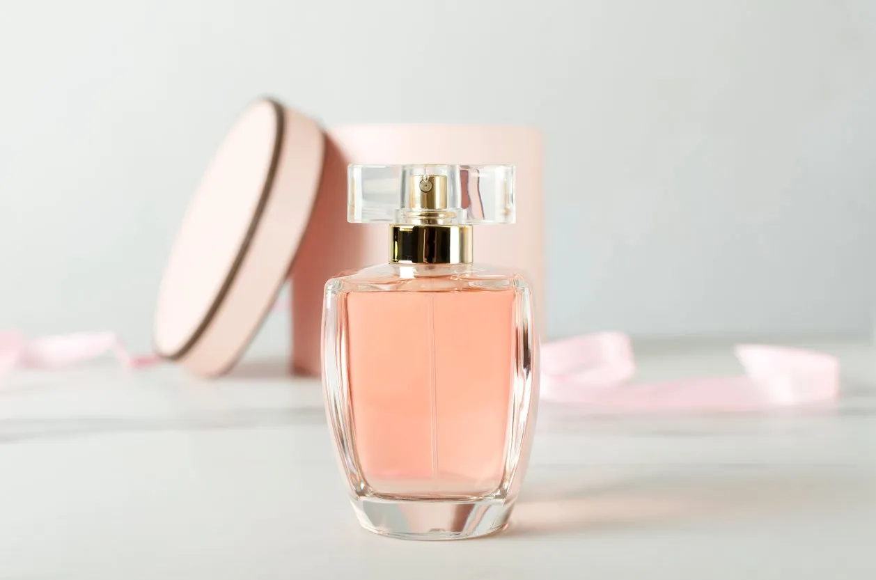 close up of glass bottle of perfume and pink round gift box on the white surface against white background