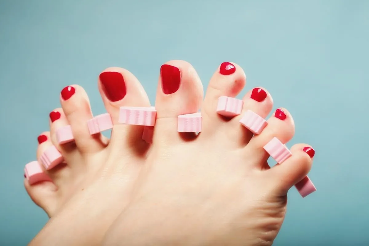 foot pedicure applying woman's feet with red toenails in pink toe separators blue background