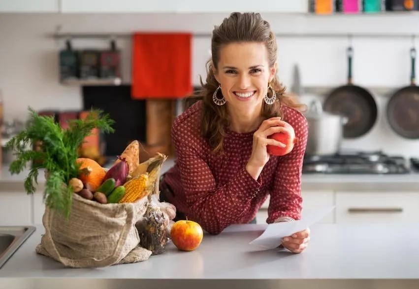 portrait de heureux jeune femme au foyer, tenant des chèques d'épicerie dans la cuisine