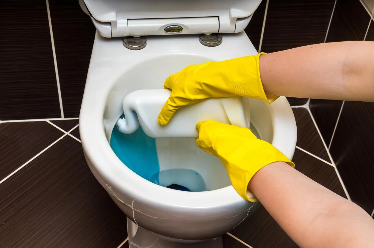 woman in yellow rubber gloves is cleaning toilet bowl using detergent