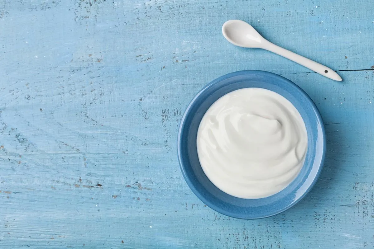 greek yogurt in blue bowl on rustic wooden table top view