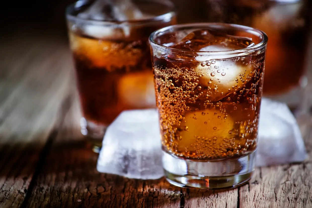 alcoholic cocktail with cola and whiskey and ice cubes, vintage wooden background, selective focus