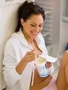 femme assise mangeant devant un réfrigérateur ouvert