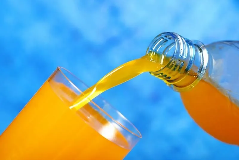 orange juice pouring in a glass over blue background like a concept for summer drink
