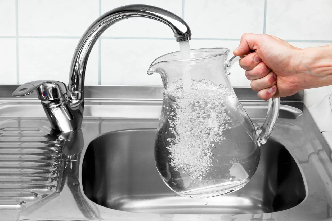 hand holding a pitcher of water being poured from the kitchen faucet