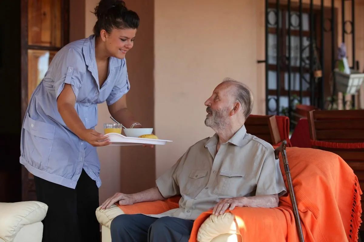 nurse or helper in residential home giving food to old senior man