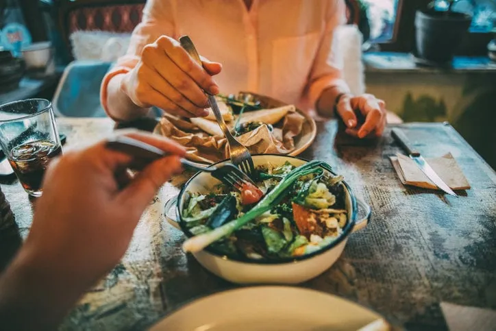 woman taking some of her boyfriend's salad on lunch at a restaurant