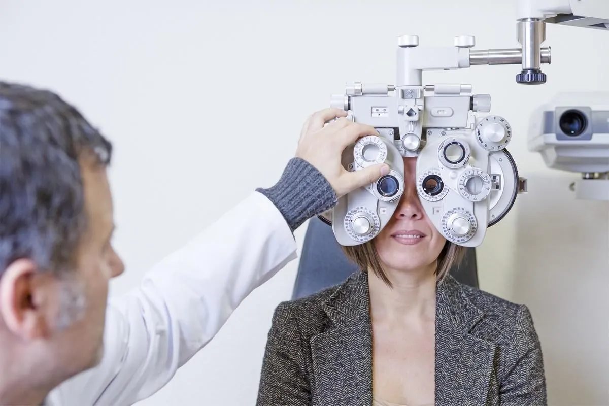 male optometrist is calibrating the optical phoropter to exam the eyesight to a young patient woman focus on the phoropter center