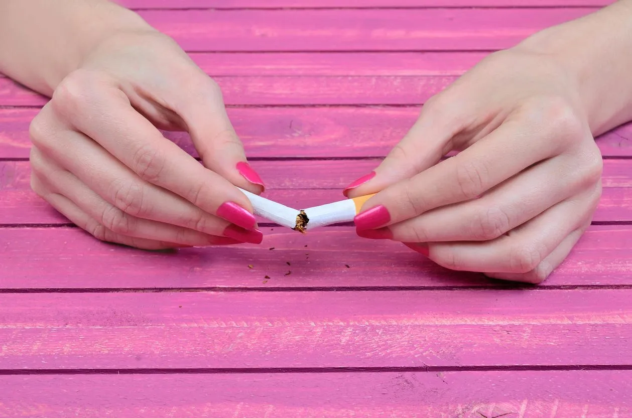 woman hand crush a cigarette on pink wooden table