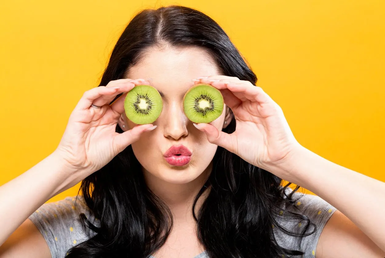 happy young woman holding kiwis on a yellow background