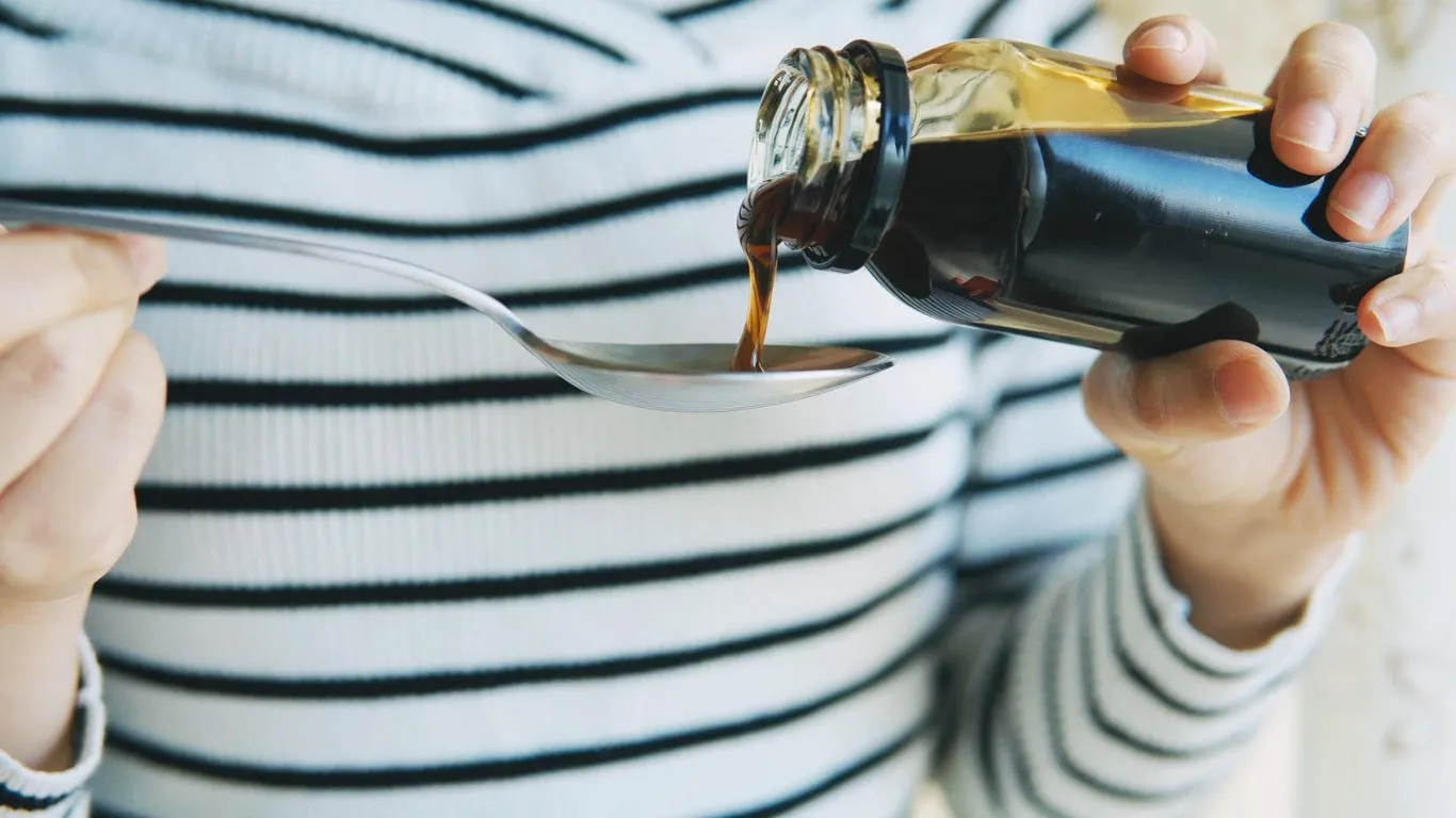 healthcare, people and medicine concept - woman pouring medication or antipyretic syrup to spoon