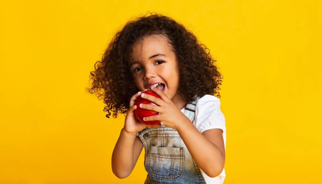 vitamin snack little girl biting red apple over yellow background