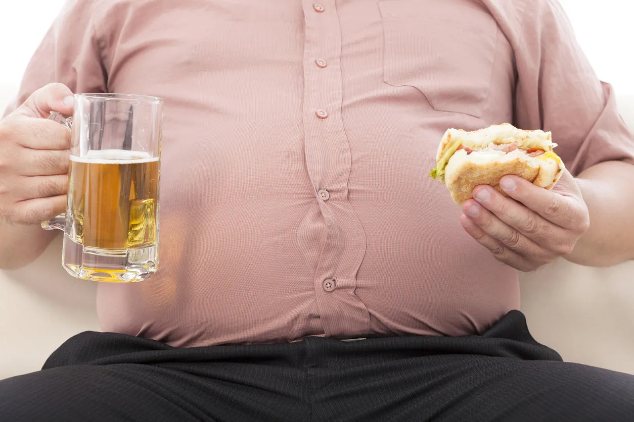 fat business man holding beer mug and hamburger on a sofa