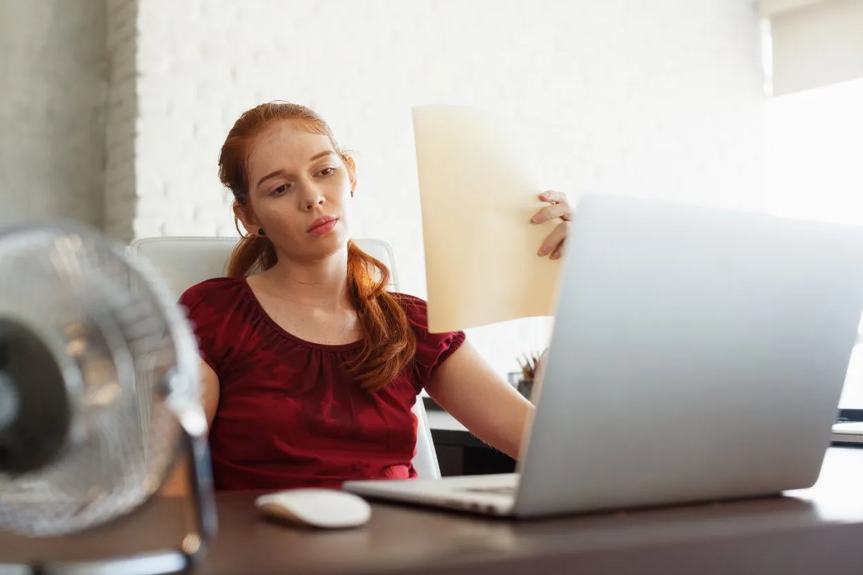 portrait of young redhead woman working with computer laptop in office at summer during heatwave the temperature is hot and the hair conditioner is broken the girl sweats and feels exhausted