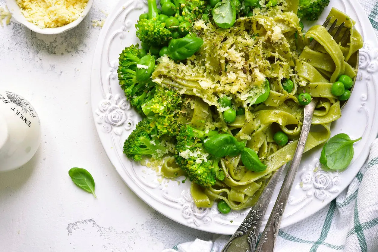 tagliatelle aux épinards de printemps avec brocoli et pois verts sur une assiette vintage blanche sur ardoise claire, pierre ou béton vue de dessus