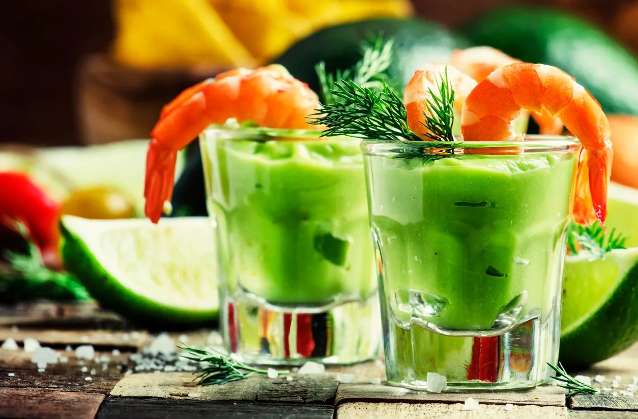 shrimp cocktail with avocado sauce and lime, vintage wooden background, selective focus