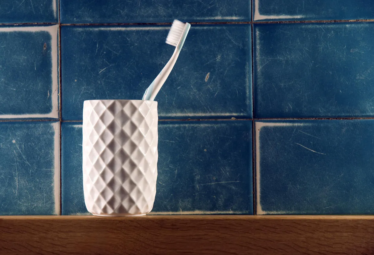toothbrush in a container sitting on a wooden shelf in front of a tiled wall