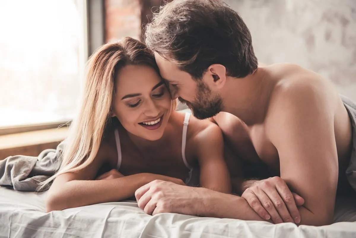 beautiful couple is smiling and hugging while spending time together in bed at home