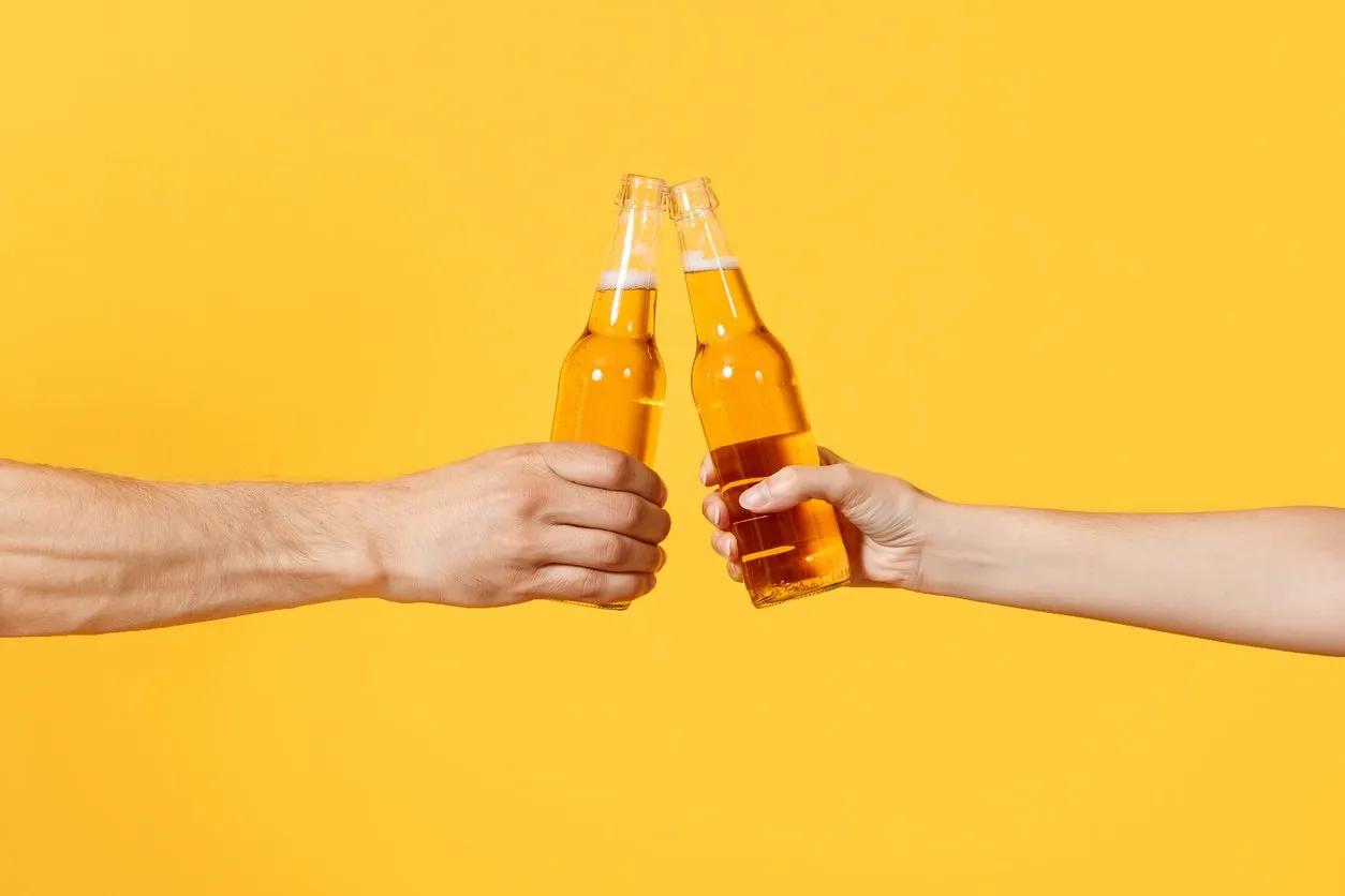 close up cropped of woman and man two hands horizontal holding lager beer glass bottles and clinking isolated on yellow background sport fans cheer up friends leisure lifestyle concept copy space