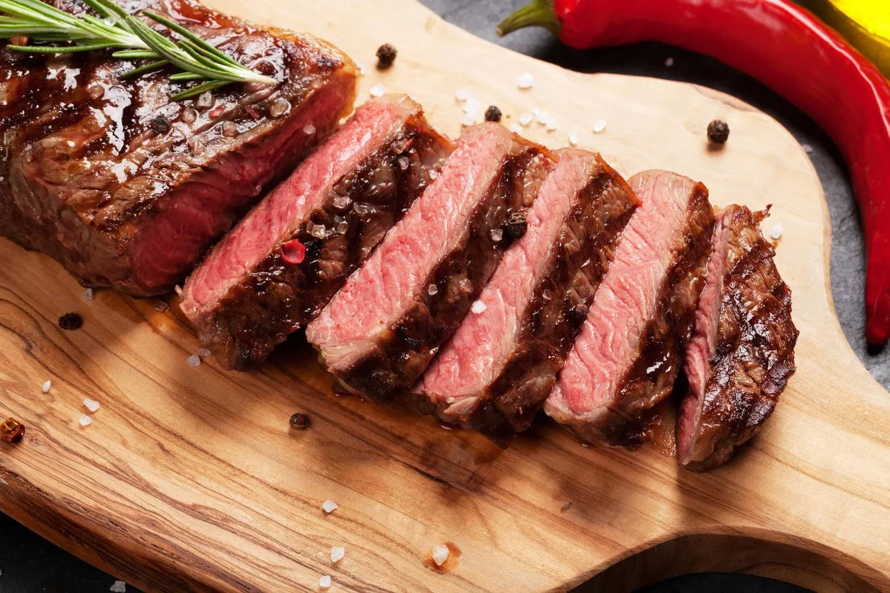 grilled striploin sliced steak on cutting board over stone table