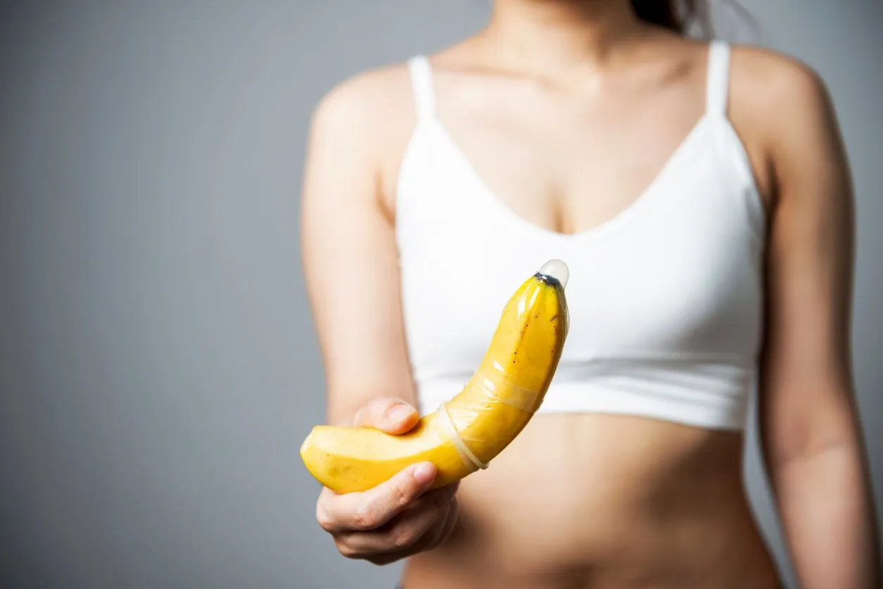female hand puts condom onto banana