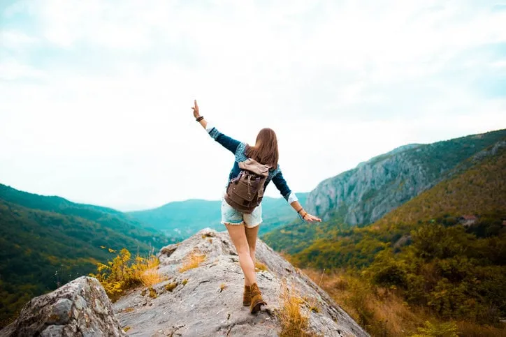 young hippie girl taking a walk on top of a mountain and enjoying the day rear view
