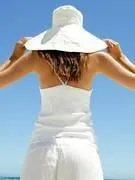 femme sur la plage, de dos, tenant son chapeau