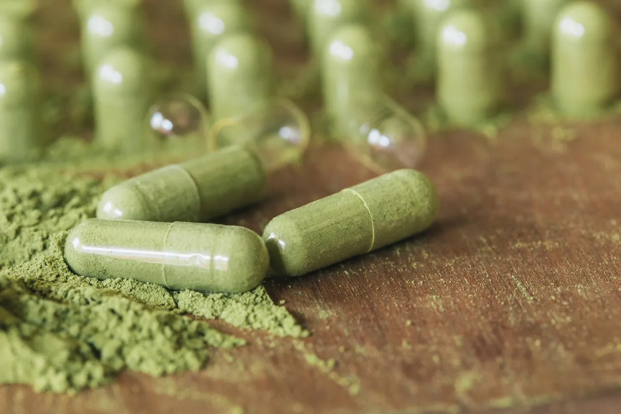 herbal medicine in capsules with green powder herbs on wooden table