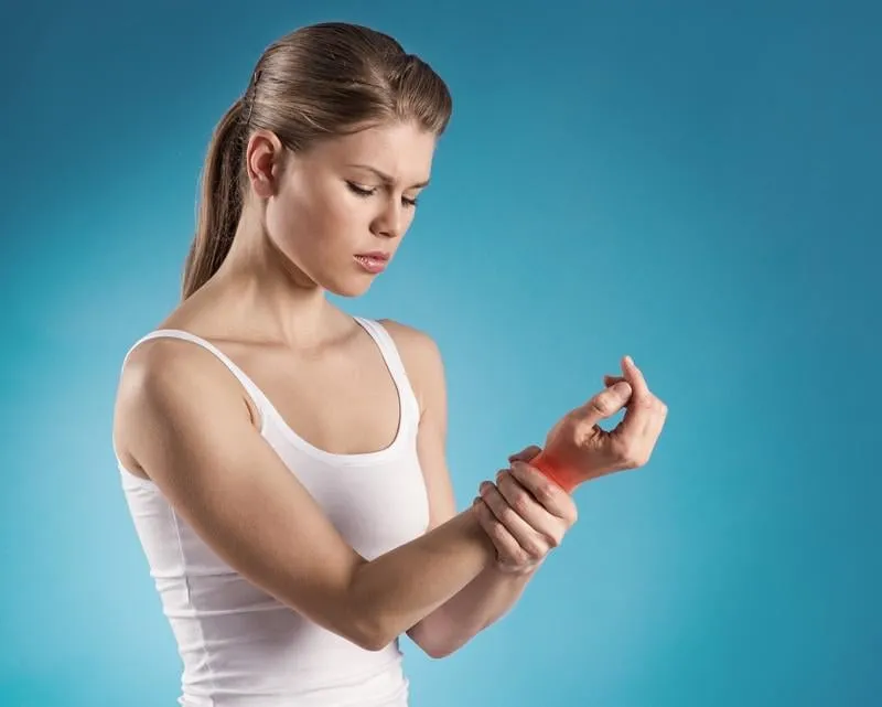 jeune femme tenant son poignet douloureux sur fond bleu