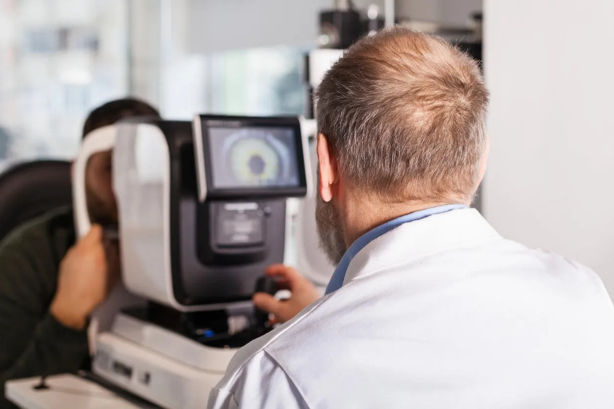 ophthalmologist examining young man with optometric machine in optics store