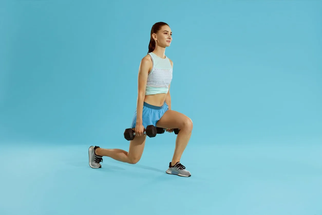 fitness workout woman exercising with gym weight at studio full length shot of fit girl in sports wear doing lunge exercise with dumbbells on colorful blue background