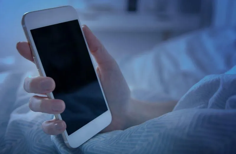 woman in bed holding smart phone at night close up, blank screen