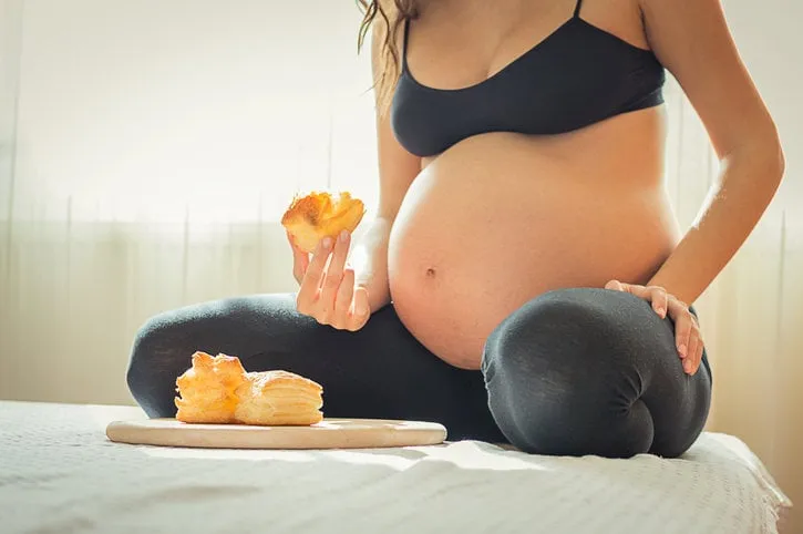 women with maternity belly eat pastry, pregnant women having breakfast on bed, women eating pastry on beautiful morning in her bed