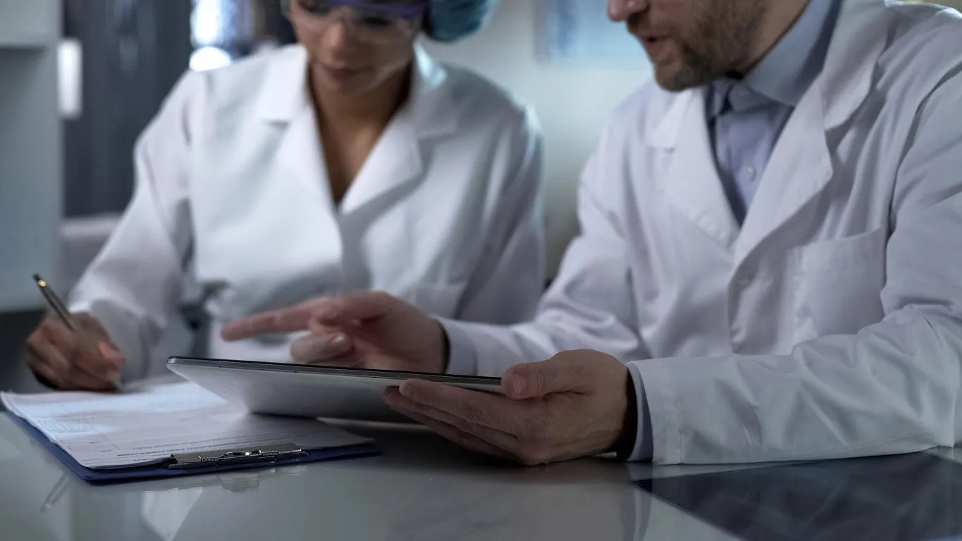 male doctor holding tablet, giving female assistant instructions to note down