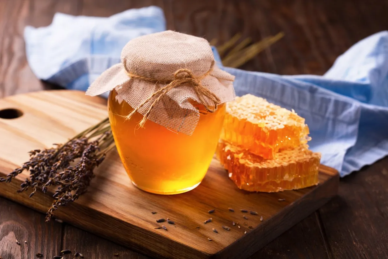 jar of liquid honey with honeycomb inside and bunch of dry lavender over old wooden table dark rustic style, selective focus