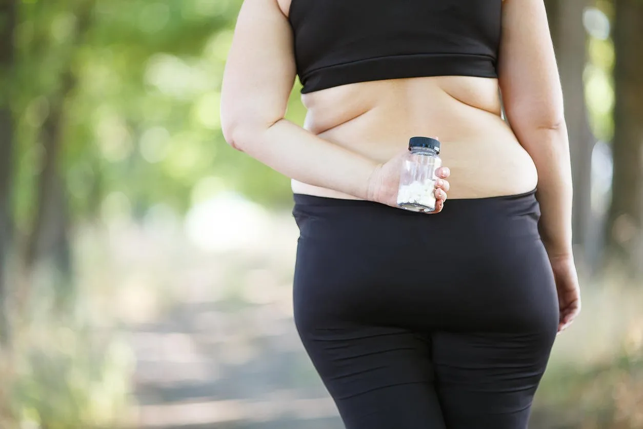 overweight fat woman hiding slimming pills behind her back unconfident, weight loosing, diet, fat burning, pharmacy, medicine concept