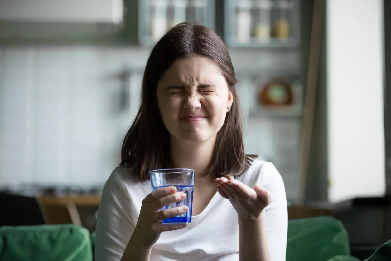 frustrated stressed young woman grimacing afraid of taking pill holding glass of water, teen girl does not like daily supplements or prescribed medication, fear of medicine side effects concept