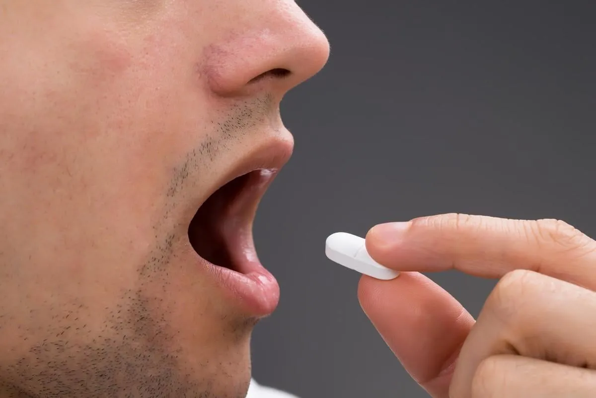 cropped image of man taking medicine against gray background