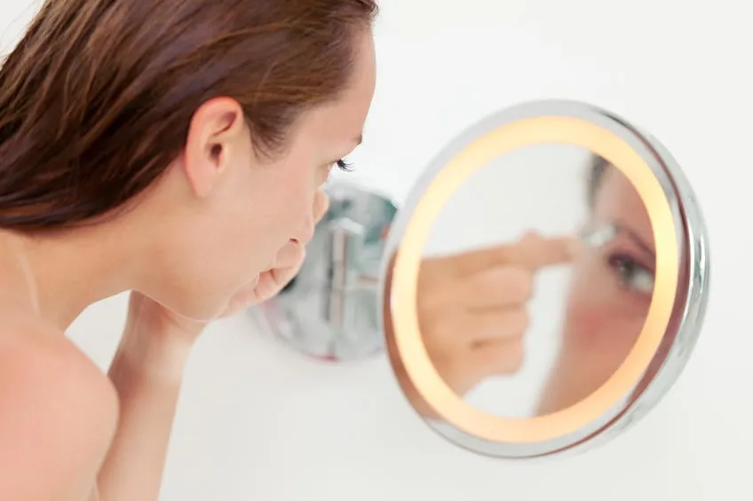 jeune femme tweez ses sourcils devant un petit miroir de salle de bain
