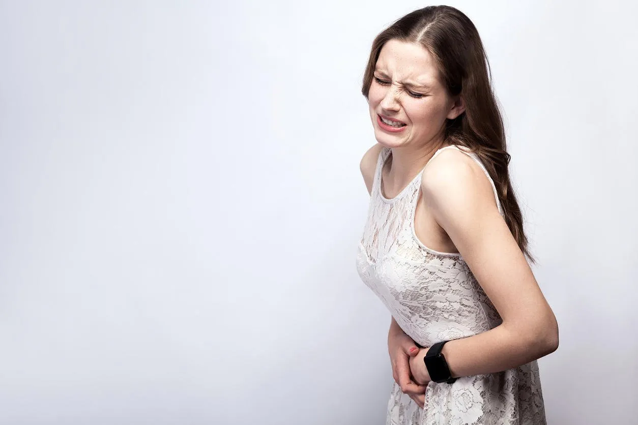 portrait of beautiful woman with freckles and white dress and smart watch with stomach pain on silver gray background healthcare and medicine concept