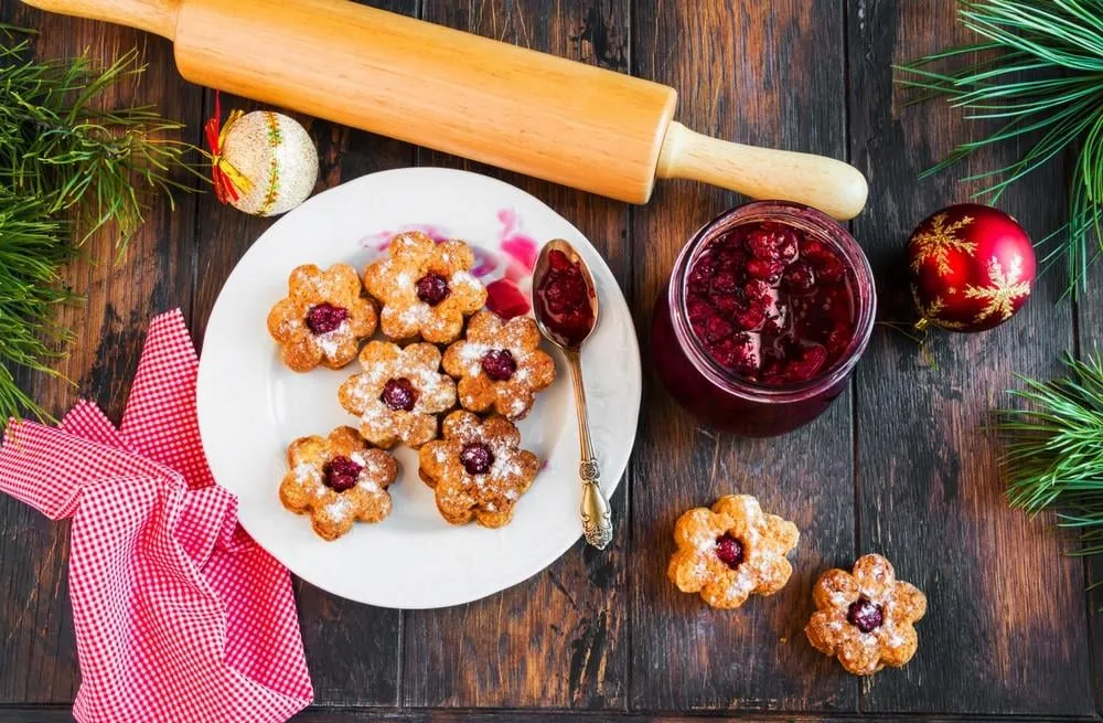 christmas linzer homemade cookies with strawberry jam on wooden background white plate, festive decoration, top view