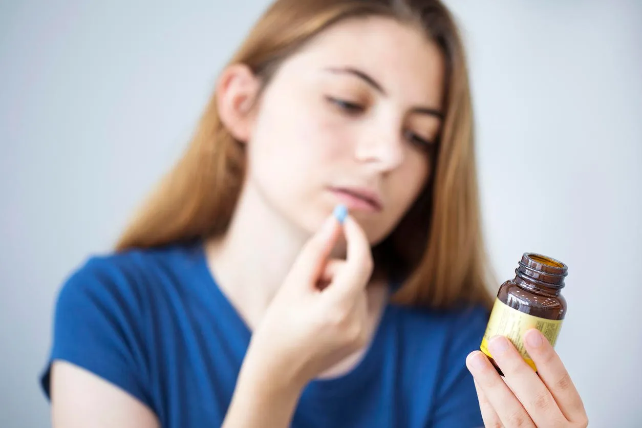young woman taking a pill while reading the bottle