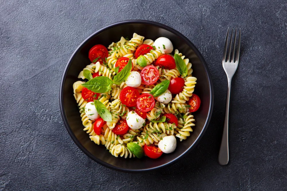 pasta fusilli with mozzarella cheese, tomatoes and basil dark background close up top view