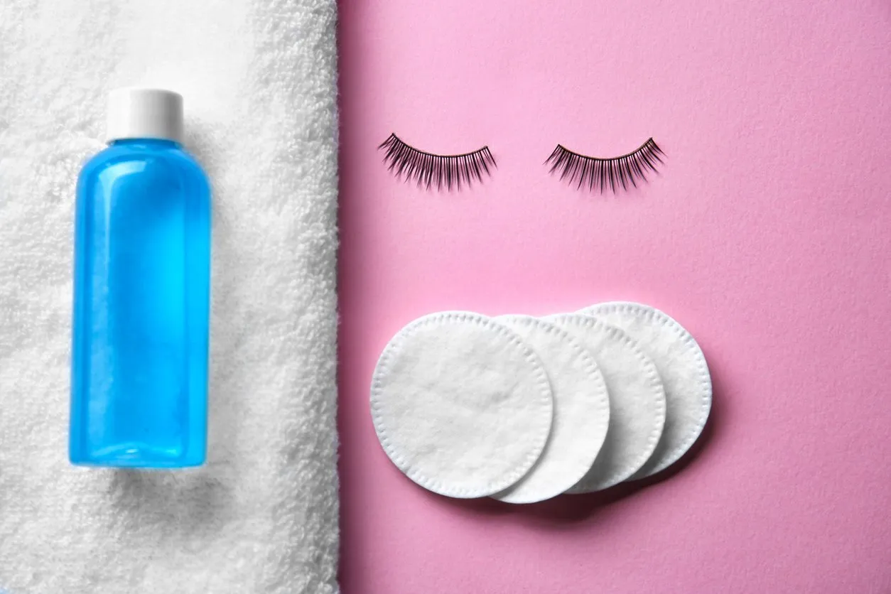 makeup remover, false eyelashes and cotton pads on color background