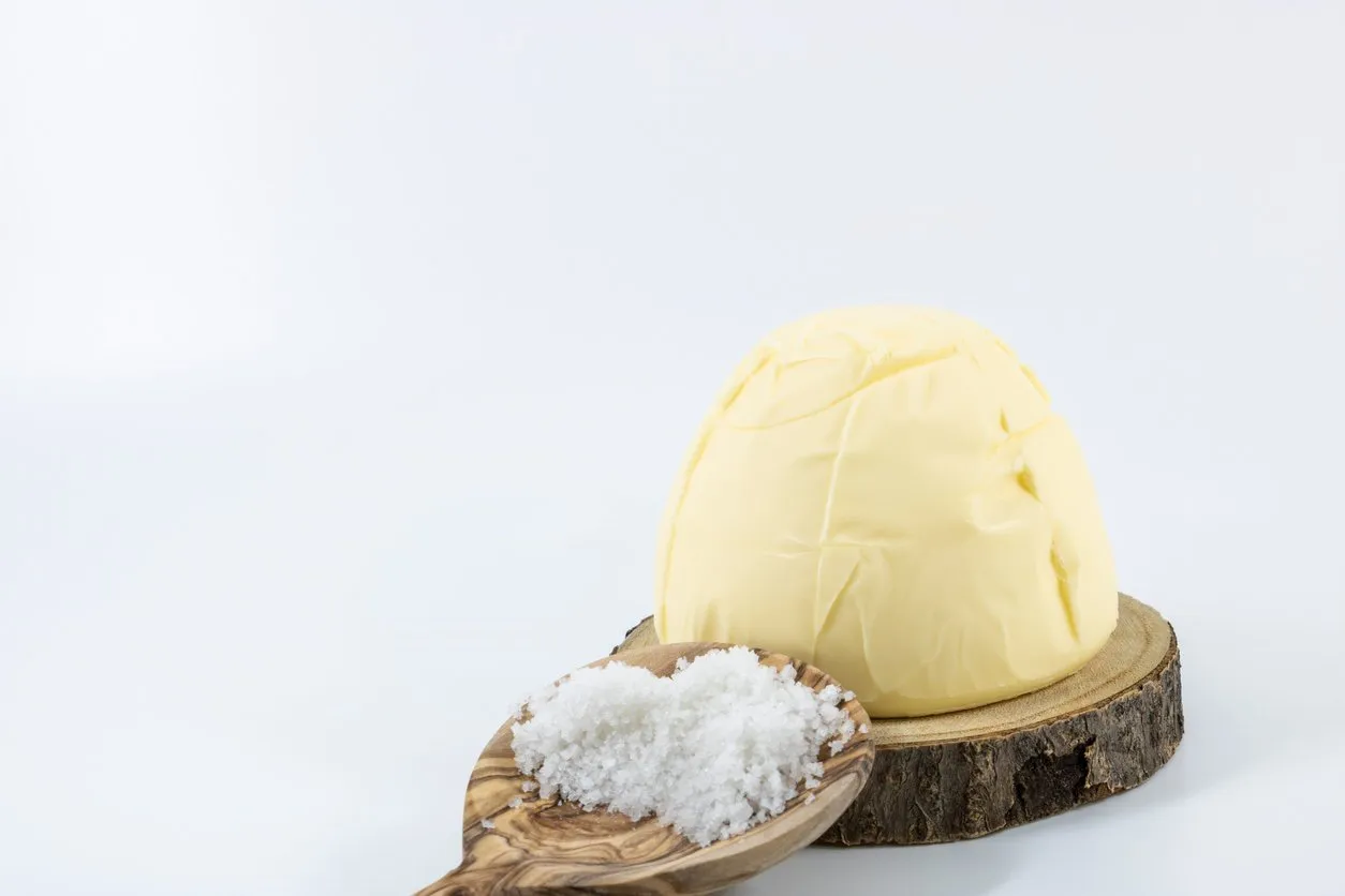 motte of salted butter churned with guérande salt on a wooden tray and a wooden spoon of big salt guérande photo studio on white background