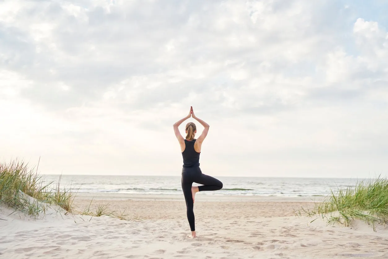 a young woman wearing gym clothes doing yoga on the beach on a sunny day