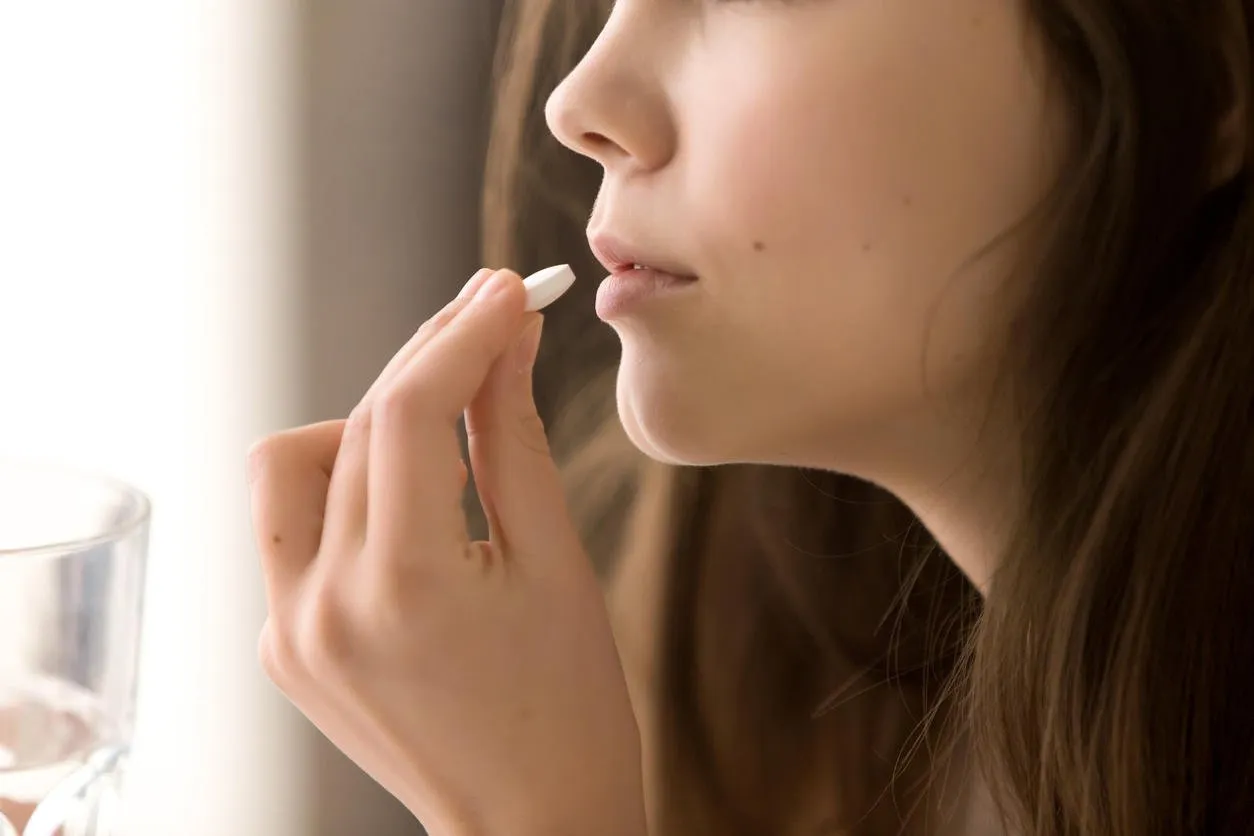 close up image of woman putting white round pill in mouth sick female taking medicines, antidepressant, painkiller or antibiotic young lady drinking contraceptives pharmacy and healthcare concept