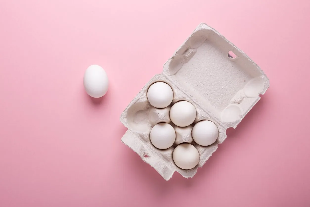 six white eggs in carton box on pink paper background top view symbol happy easter flat lay copy space